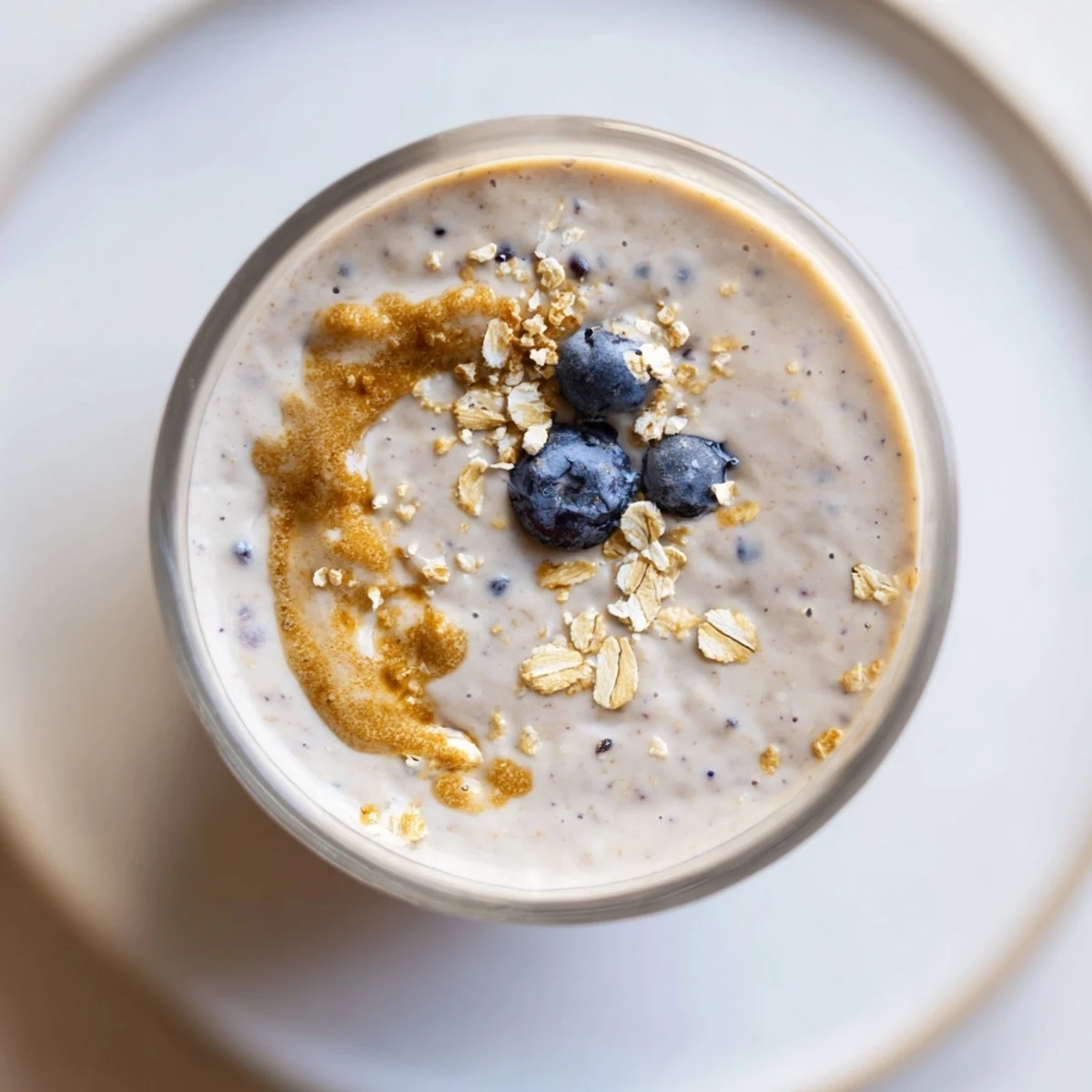 Tall glass of creamy Blueberry Brown Butter Oat Smoothie, garnished with a few fresh blueberries and a mint sprig.