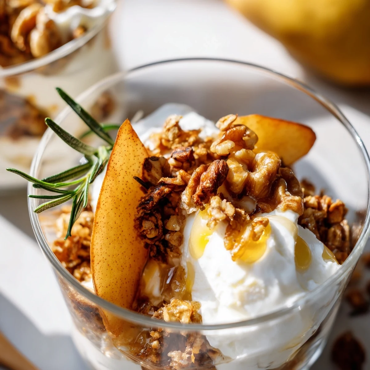 Golden roasted pear slices with rosemary and honey are layered in a clear glass with creamy Greek yogurt and crunchy granola.