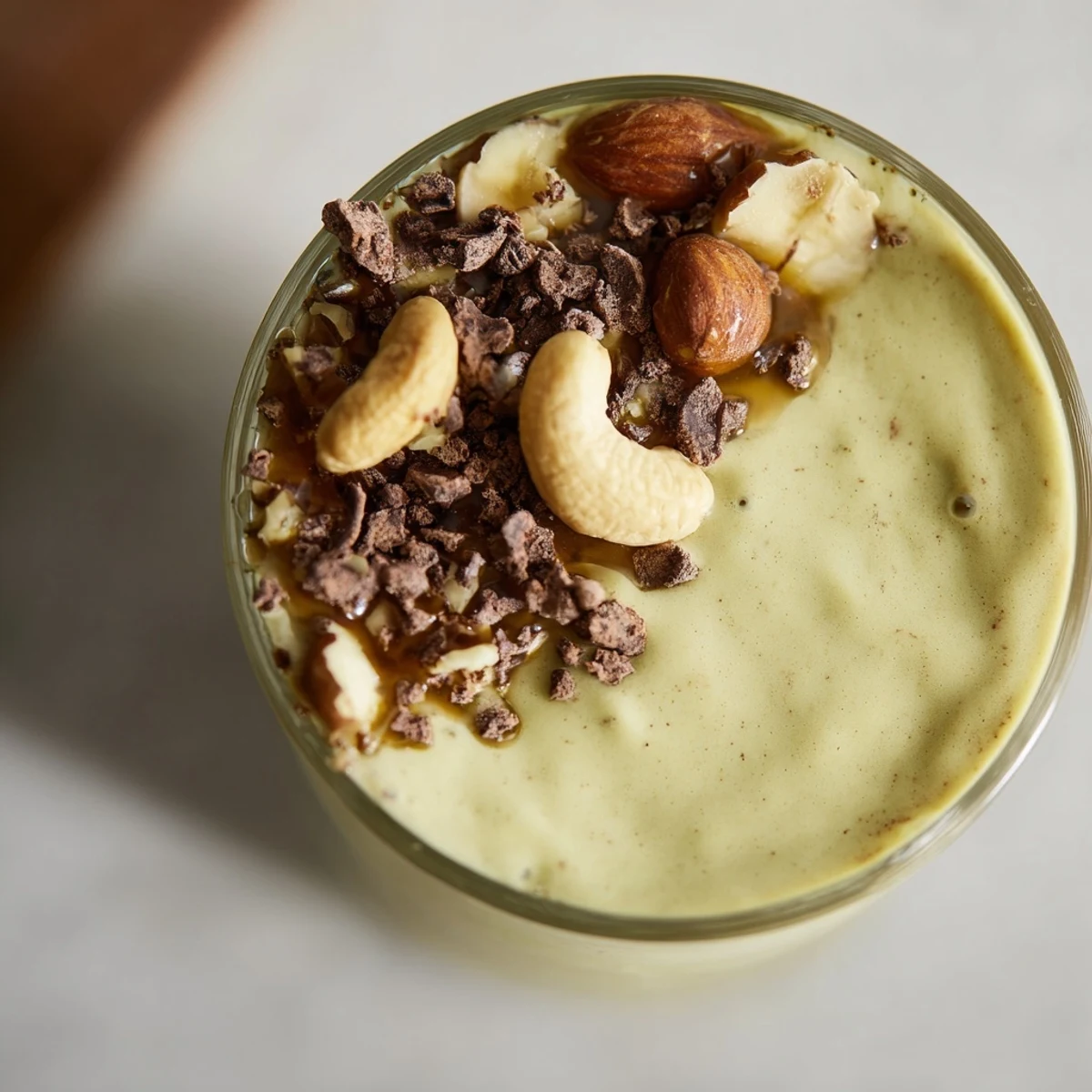 Healthy Avocado Slow Roasted Nutty Cacao Smoothie served in a tall glass with a reusable straw and banana.