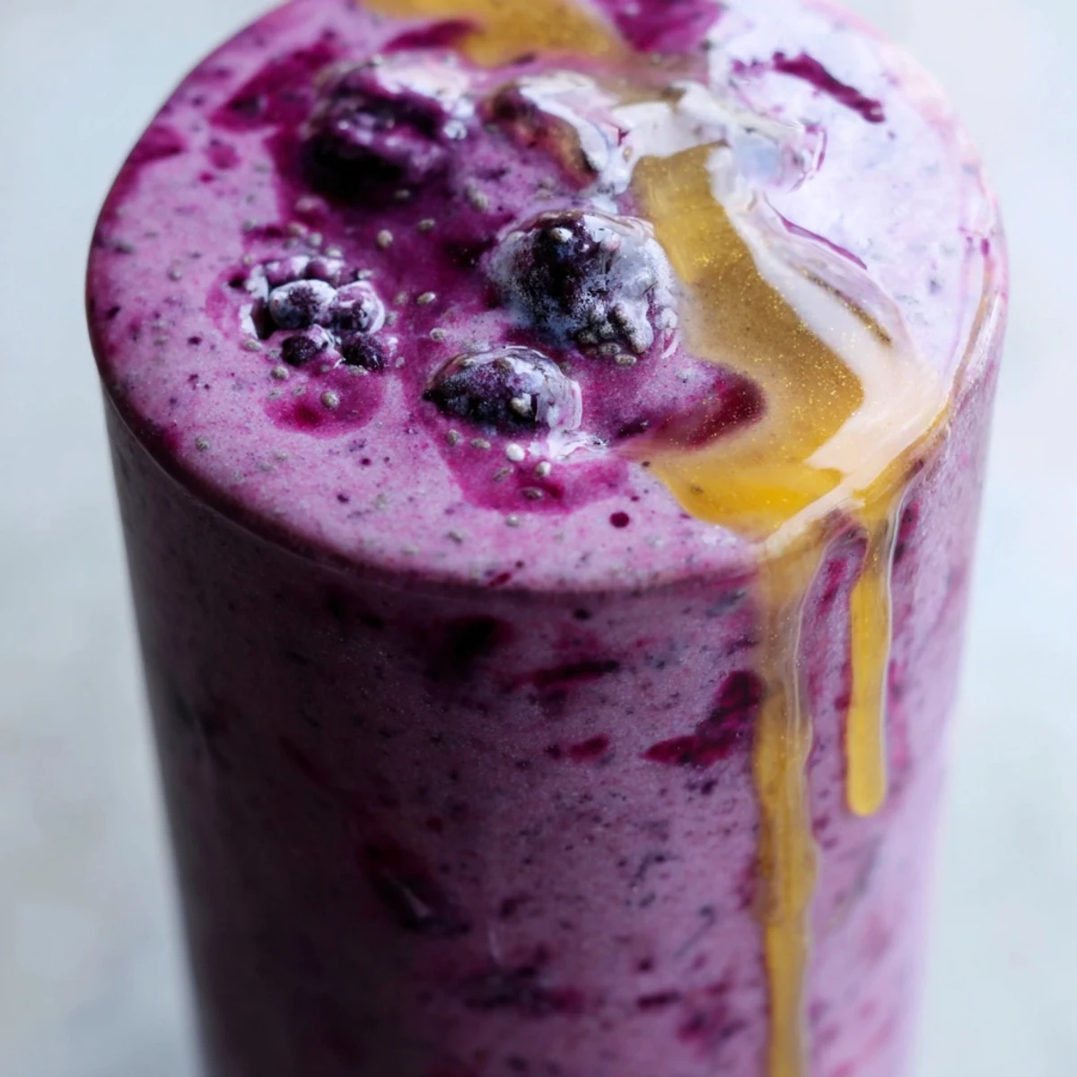 Serving two glasses of vibrant Honey Glazed Winter Berry Smoothie garnished with fresh blueberries and raspberries.