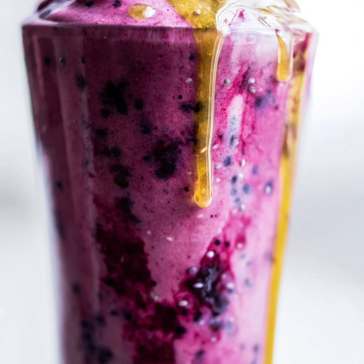 Overhead view of a frothy, purple Honey Glazed Winter Berry Smoothie next to fresh berries and honey.