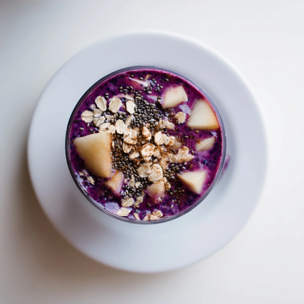 A tall glass of vibrant pear and spice blueberry oat smoothie with fresh blueberries on top.