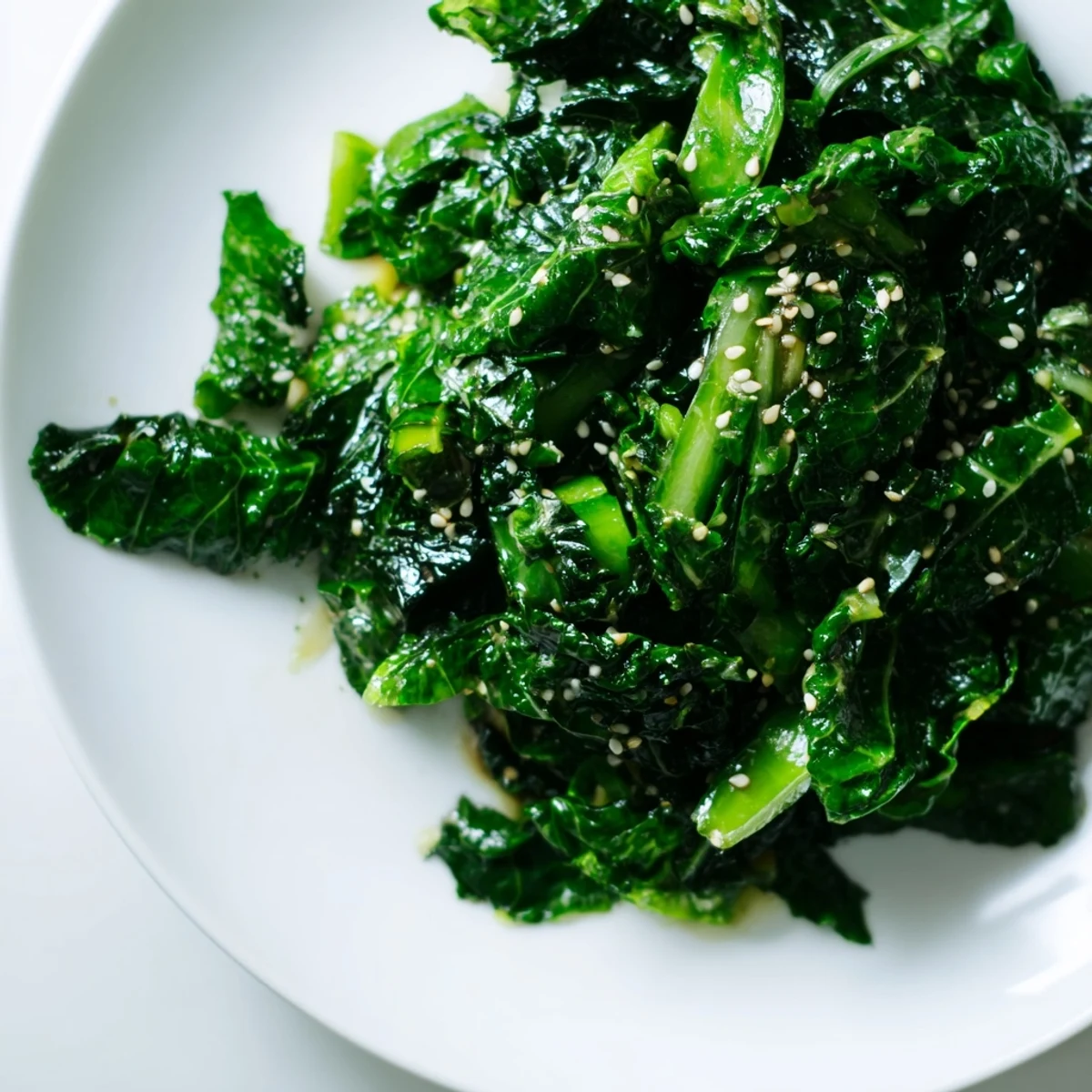 A close-up of Braised Winter Greens with Warming Miso Glaze, showcasing wilted kale and Swiss chard glistening with a savory-sweet glaze, garnished with sesame seeds and scallions.