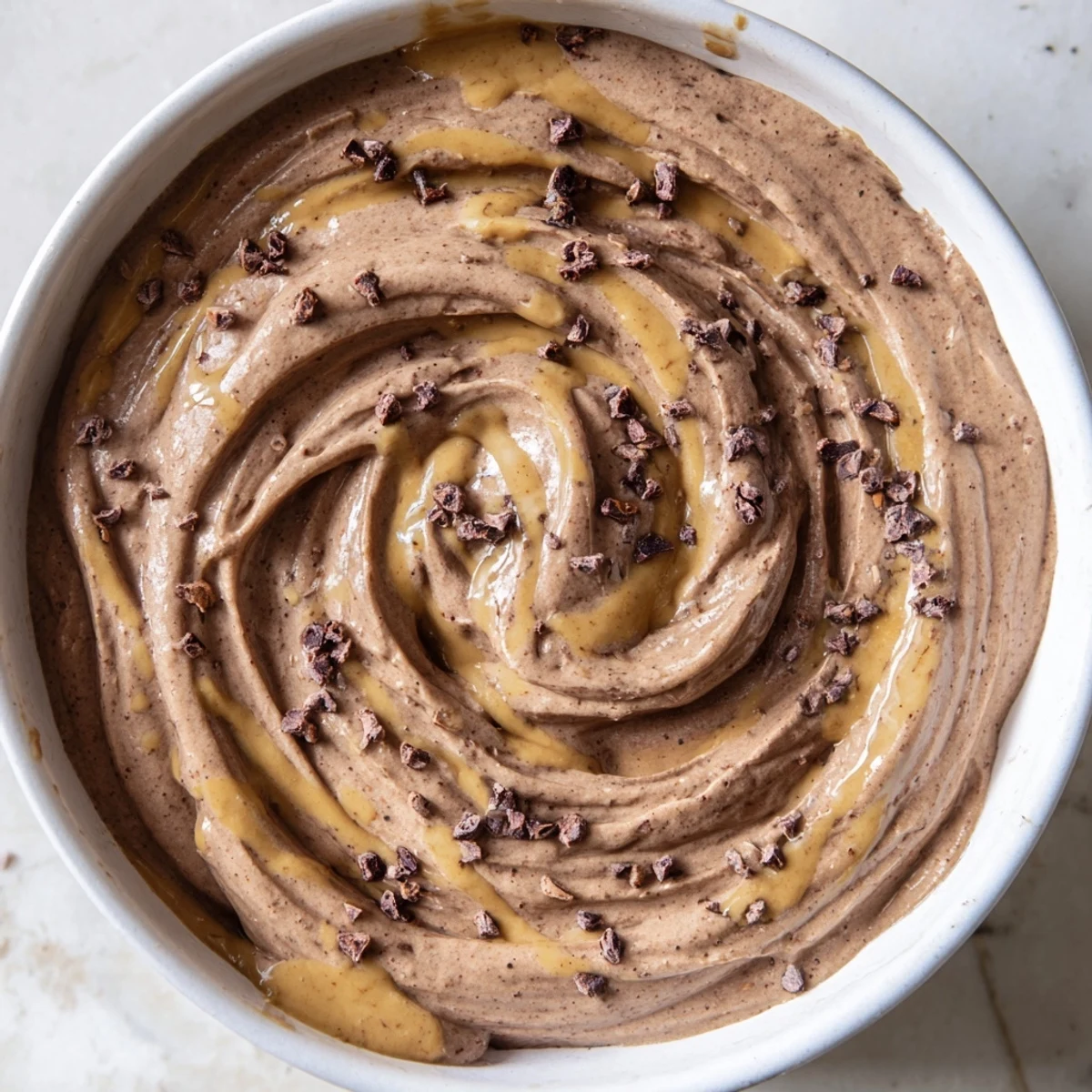 A close-up of smooth Immune Boosting Cocoa Banana Nice Cream in a white bowl, garnished with cinnamon and cacao nibs.  