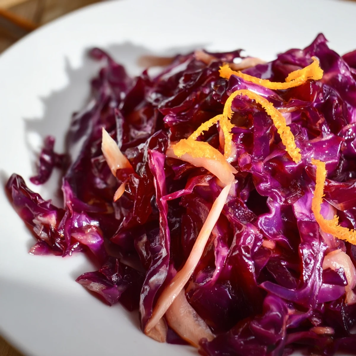 A bowl of Braised Red Cabbage with an Orange Kiss, garnished with fresh orange zest and a spoon ready to serve warm.