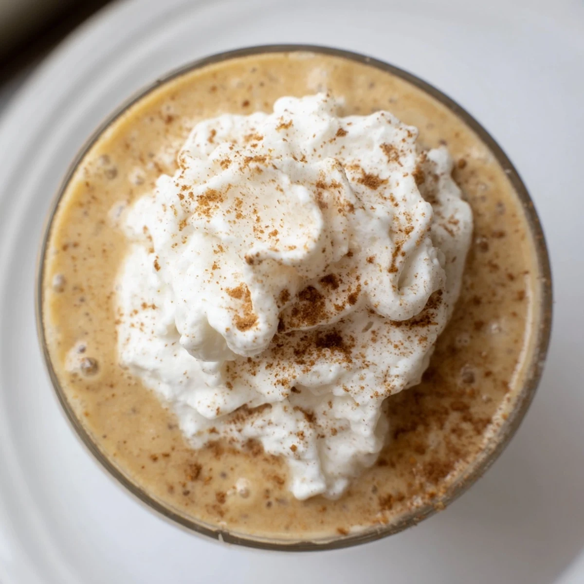 Two servings of pumpkin spice smoothie in tall glasses, garnished with cinnamon, showcasing the rich, orange hue of the blended ingredients.