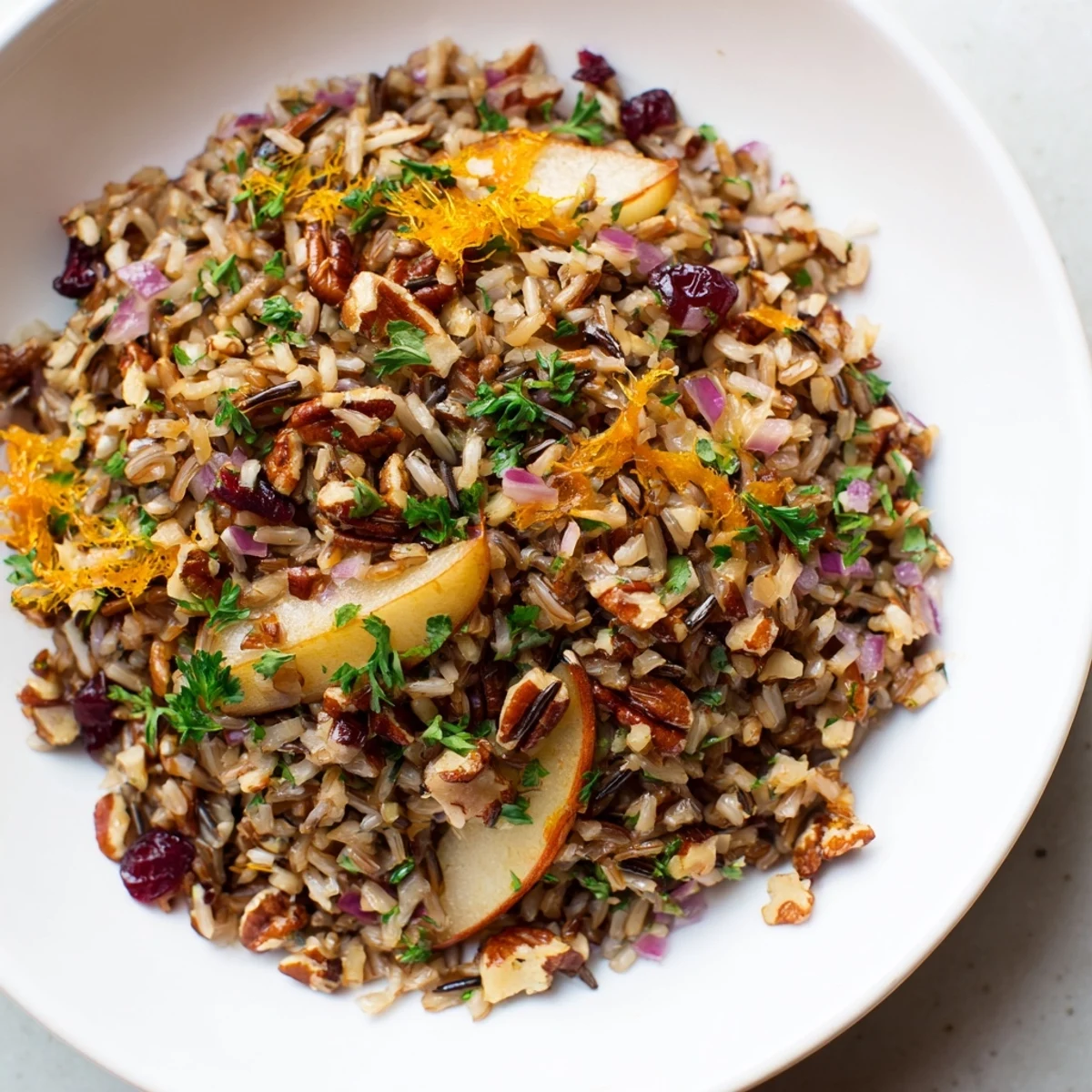 A close-up of Wild Rice Citrus Pilaf with Warm Pear and Spiced Apple in a rustic serving bowl, garnished with fresh parsley and toasted pecans.