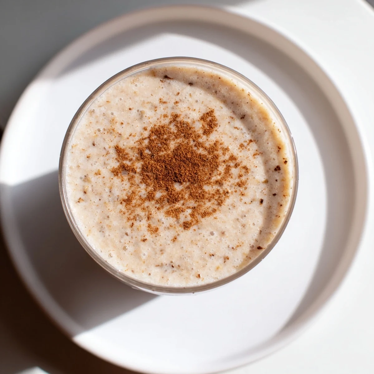 Spiced Apple Oat Smoothie garnished with oats and a cinnamon stick beside fresh apple slices.