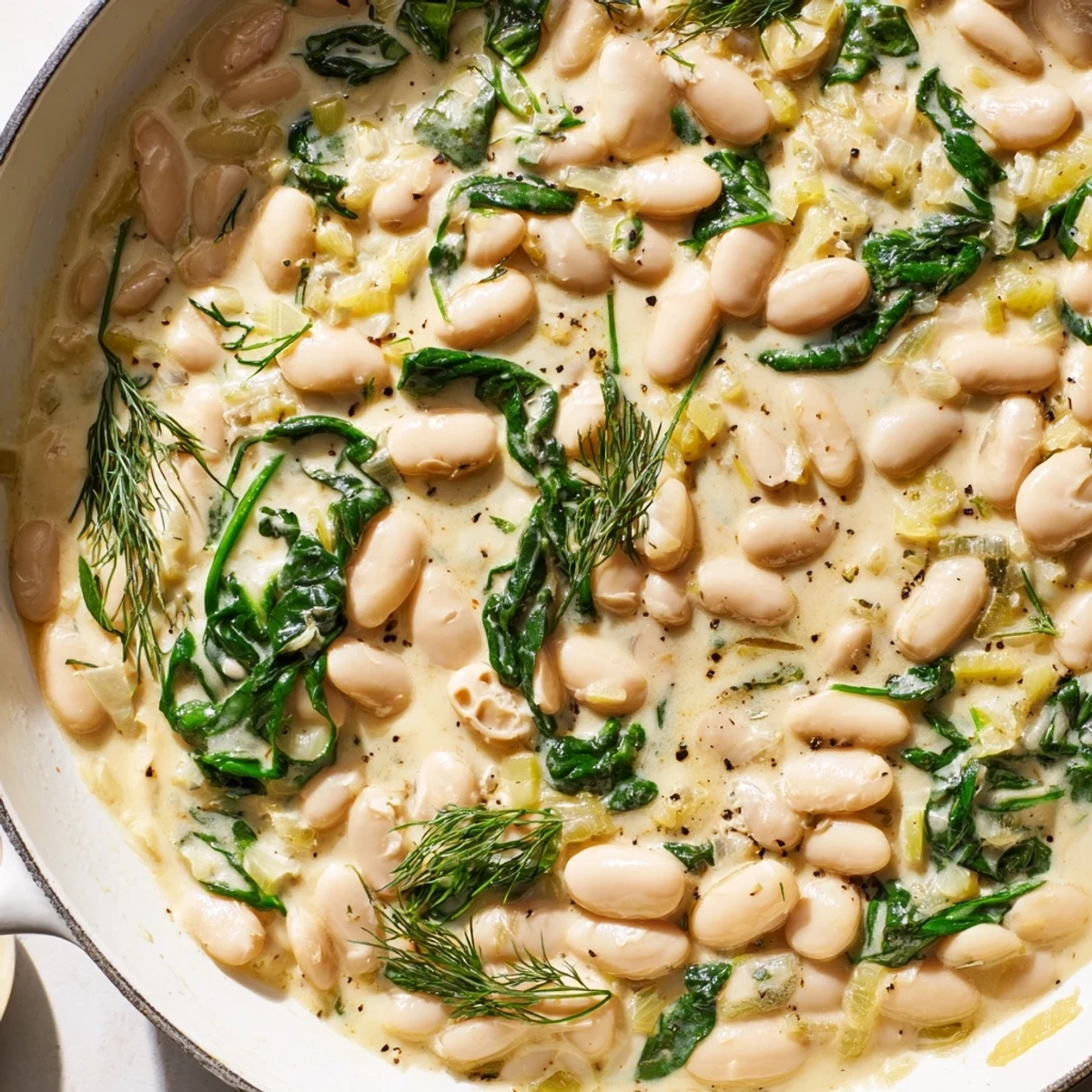 A close-up of Creamy White Bean and Herb Skillet with a rich, herbed sauce, garnished with dill and lemon wedges.