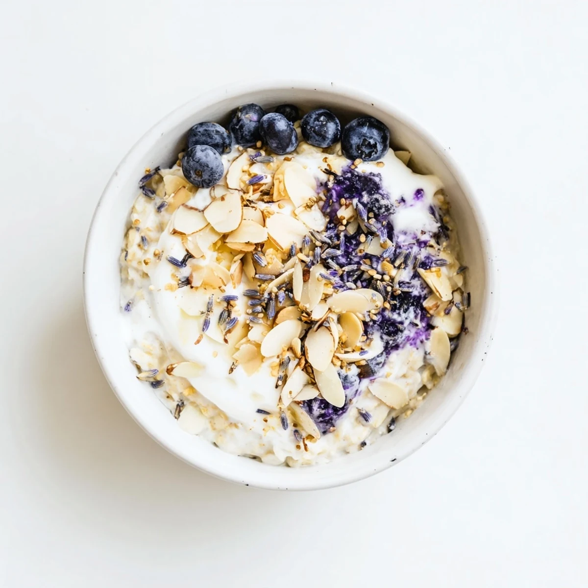 A warm Blueberry Lavender Oat Breakfast Bowl topped with Greek yogurt, toasted almonds, and coconut flakes, served beside a steaming mug.