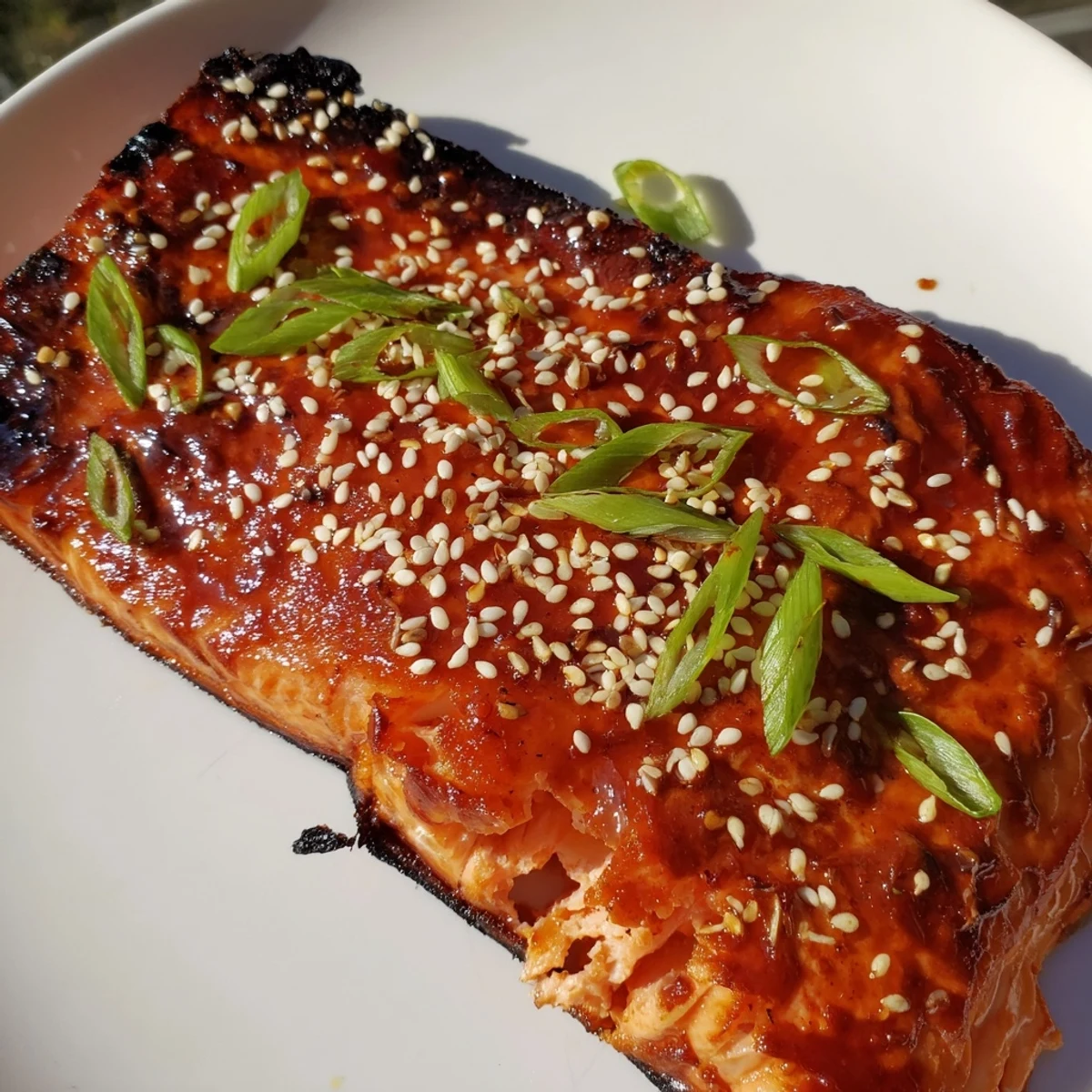 Freshly broiled Gochujang Glazed Salmon shows off its sticky, spicy-sweet sauce, garnished with sesame seeds and scallions on a ceramic dish.