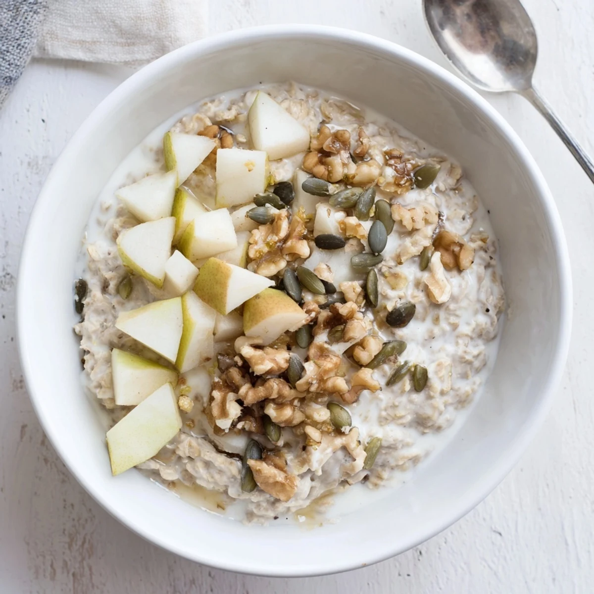 A chilled breakfast bowl of oats and yogurt layered with sweet pears and pumpkin seeds.
