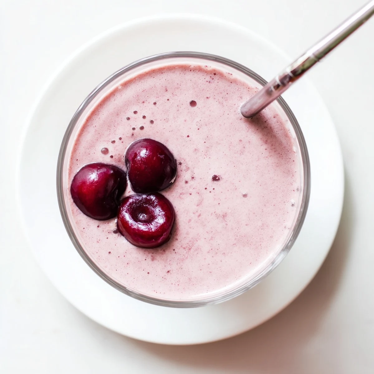 Creamy cherry vanilla protein smoothie poured into a glass with fresh whole cherries on top