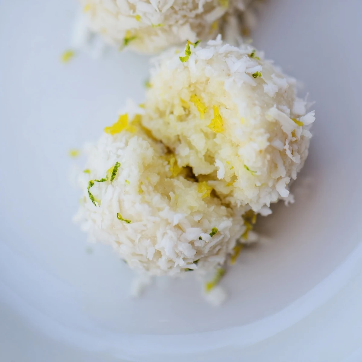 White coconut-coated Lemon Coconut Bliss Bites arranged on a wooden board with fresh lemon slices