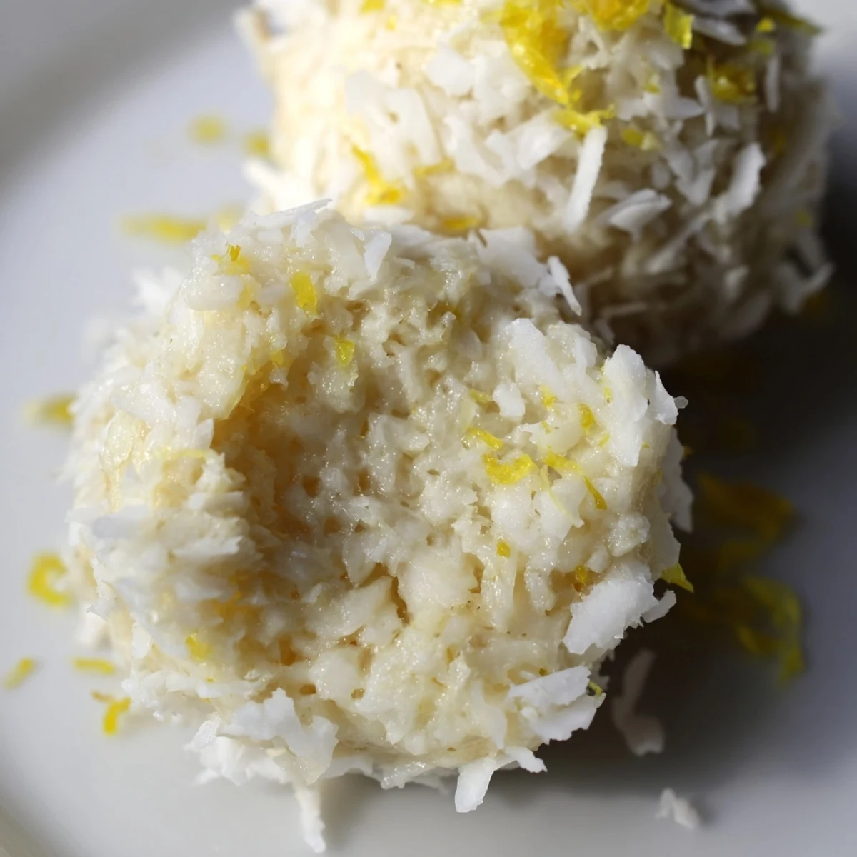 Golden brown Lemon Coconut Bliss Bites dusted with shredded coconut on a white ceramic serving plate