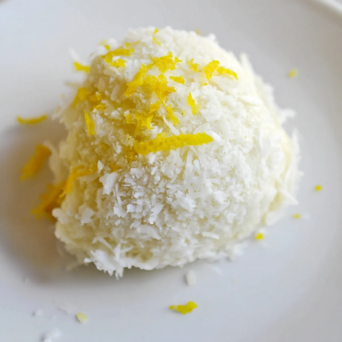 Close up of round Lemon Coconut Bliss Bites rolled in coconut with bright yellow lemon zest visible