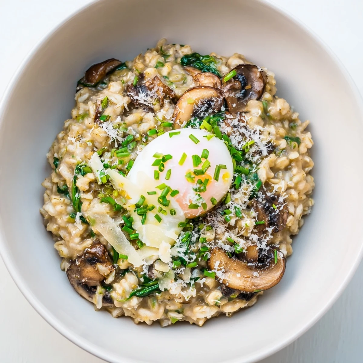 Warm breakfast bowl featuring tender spinach mushrooms and creamy oats sprinkled with nutritional yeast and fresh herbs