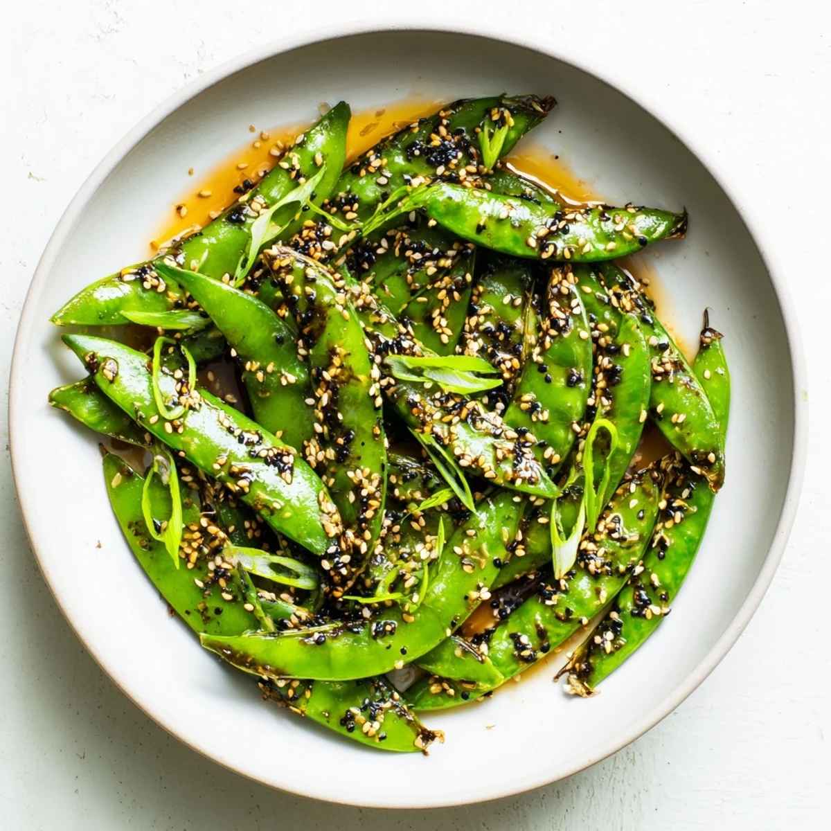 Golden roasted snap peas with sesame crunch topping garnished with fresh green onions