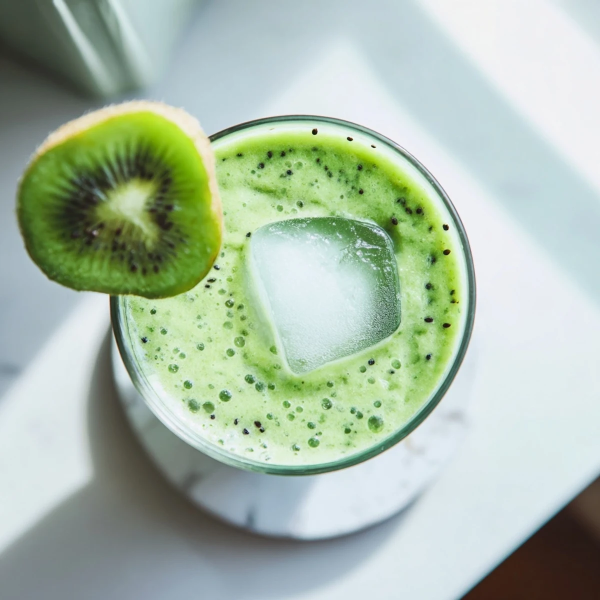 Glass of vibrant green kiwi spinach coconut smoothie garnished with fresh kiwi slices on wooden table