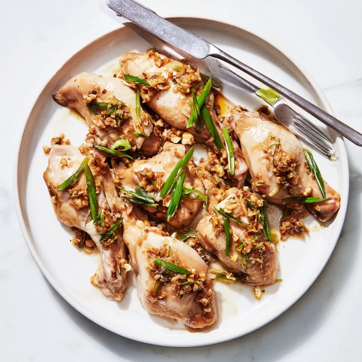 Tender ginger scallion steamed chicken arranged on a white plate glistening with savory oil-based sauce