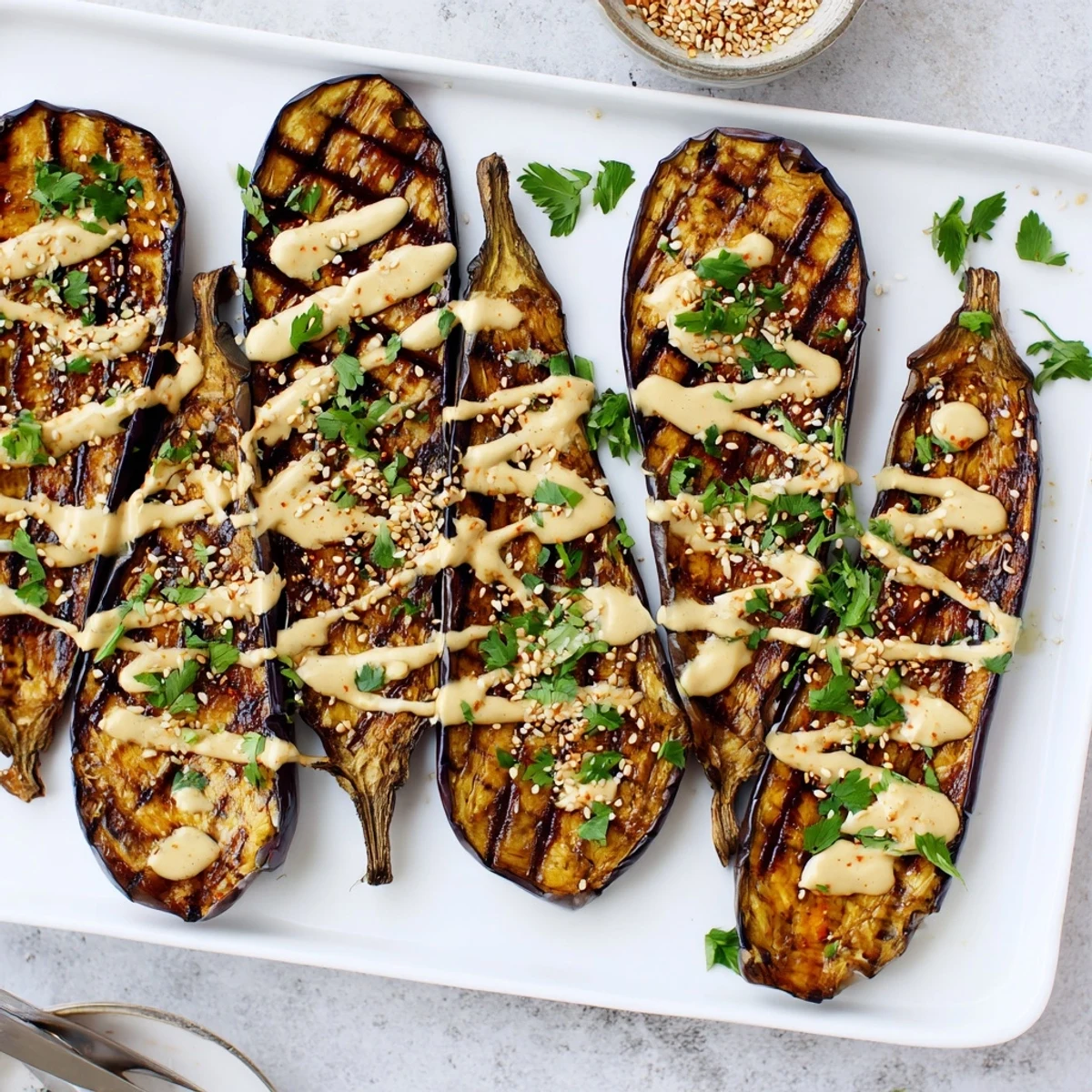 Tender caramelized eggplant topped with rich tahini drizzle and sesame seeds on a serving platter