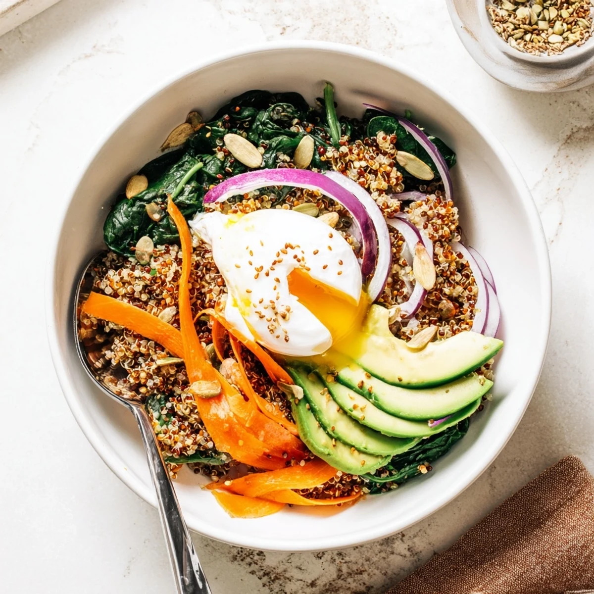 Golden poached egg rests atop sautéed spinach and sweet grated carrots in this savory breakfast bowl with creamy avocado slices