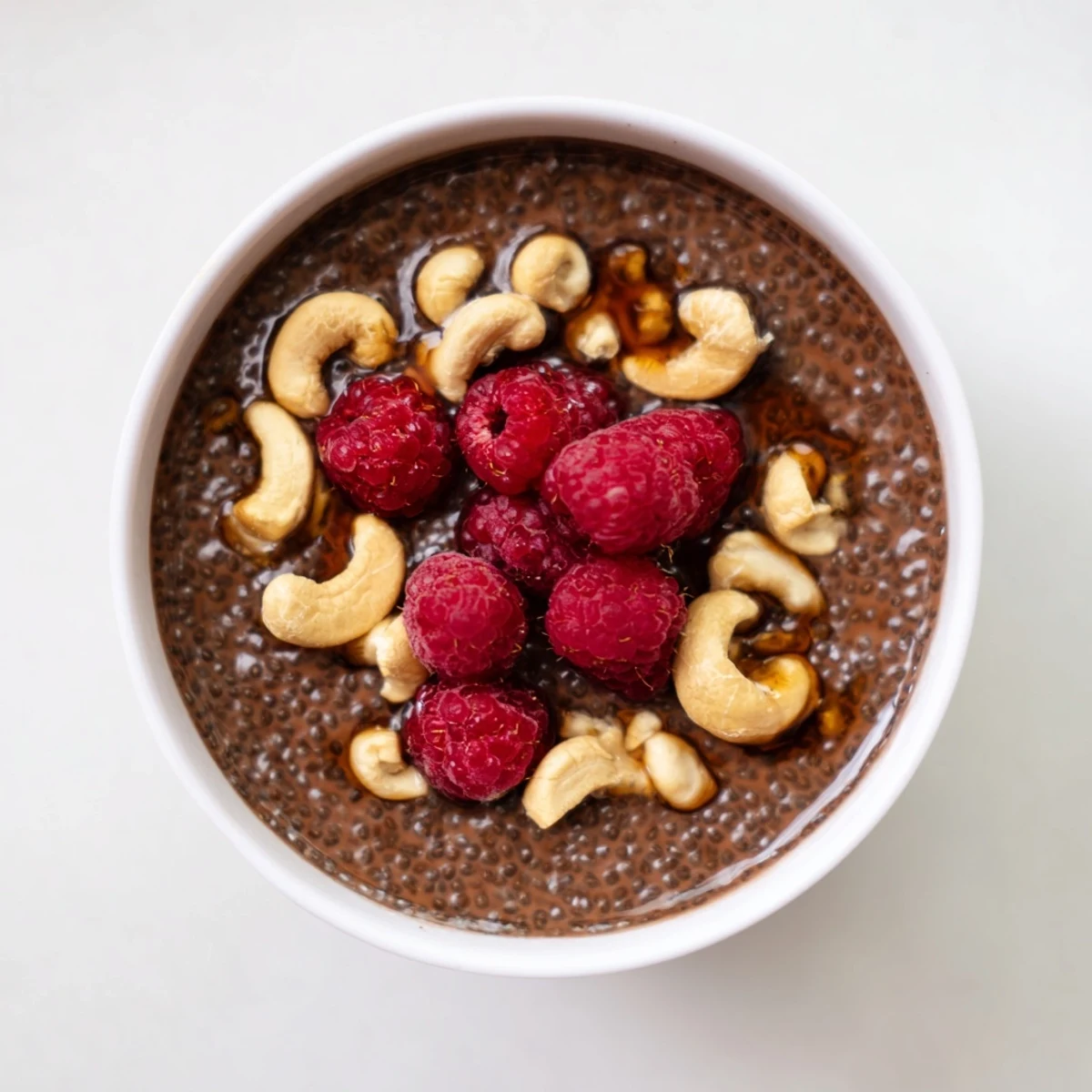 Rich cocoa cashew chia pudding topped with roasted nuts and fresh berries in a glass bowl