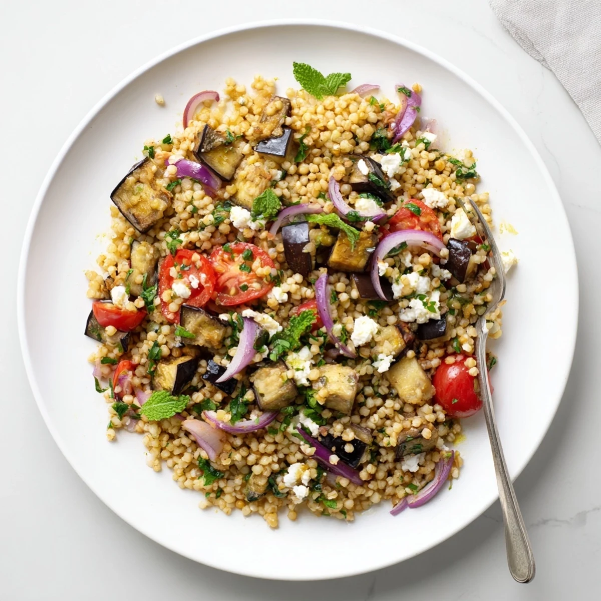 Warm bulgur wheat salad featuring smoky roasted eggplant, cherry tomatoes, and aromatic parsley mint mixture drizzled with lemon olive oil dressing