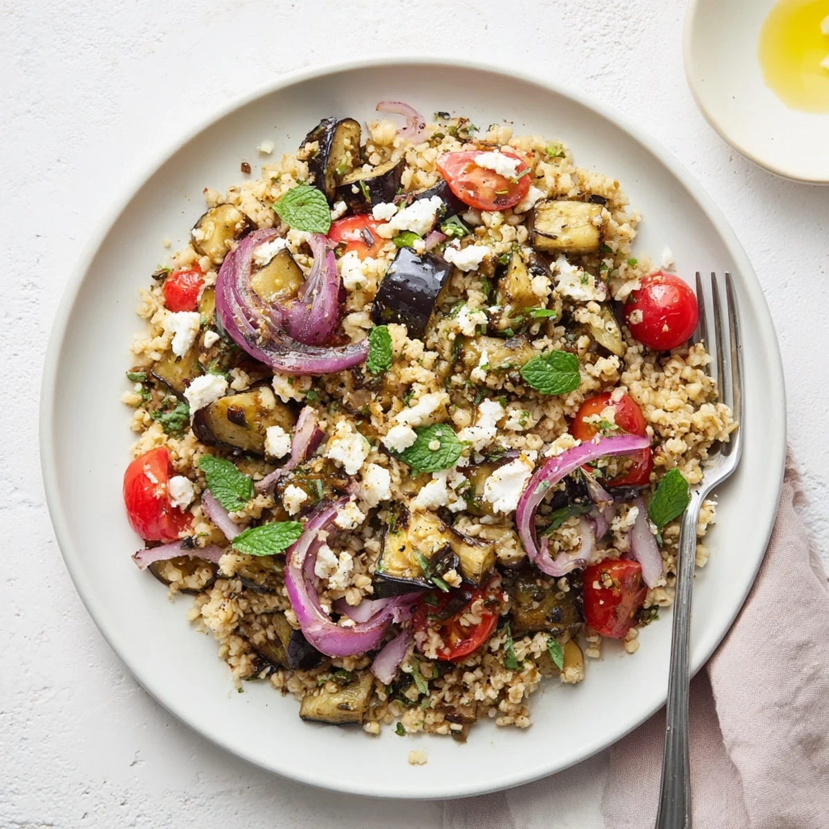 Hearty vegetarian eggplant and bulgur grain bowl topped with crumbled feta, red bell pepper, and zesty cumin paprika dressing