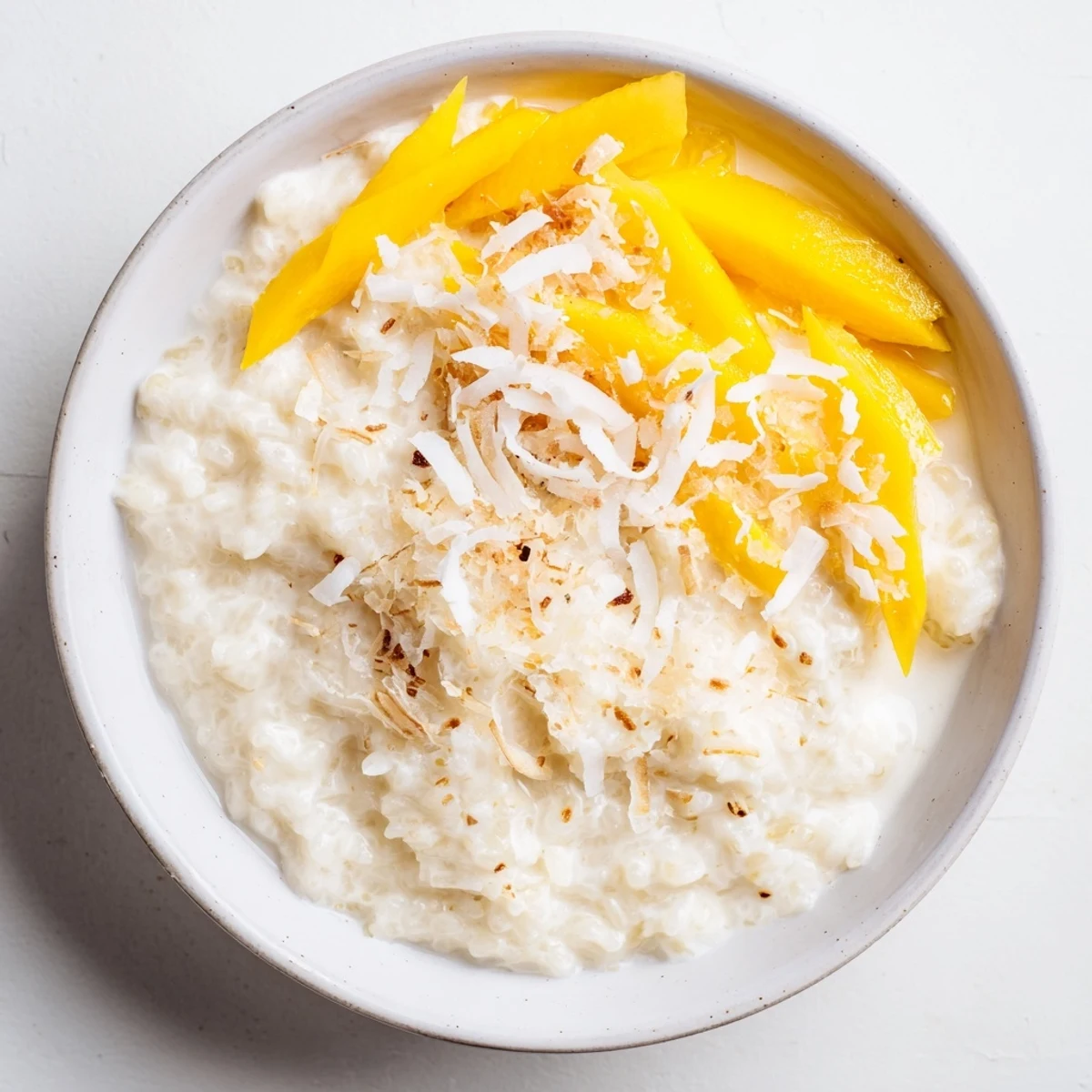 Warm vanilla coconut rice pudding topped with fresh mango slices and chopped pistachios