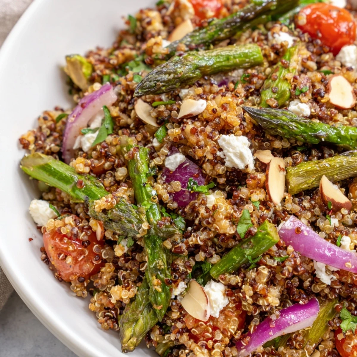 Warm quinoa and roasted asparagus salad topped with crumbled feta and toasted almonds in a white serving bowl