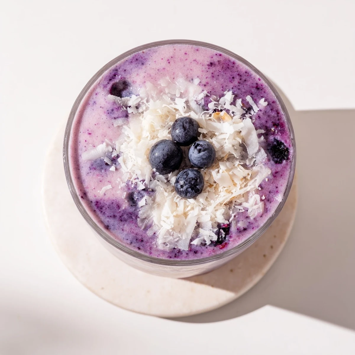 Thick purple banana blueberry coconut smoothie poured into a glass with fresh berry garnish