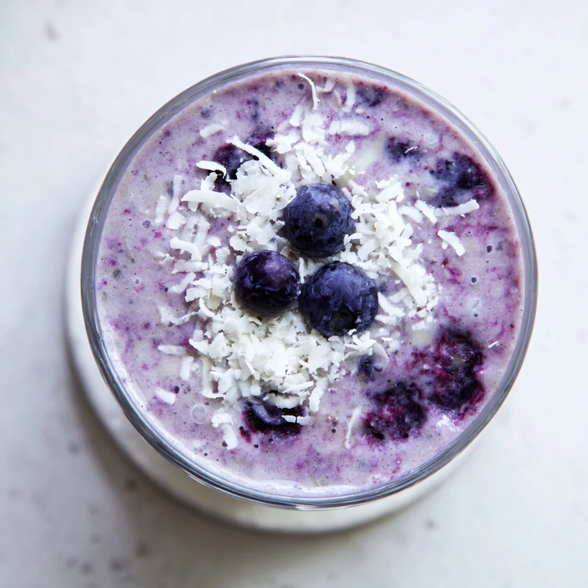 Refreshing dairy-free banana blueberry coconut smoothie topped with shredded coconut and blueberry swirl