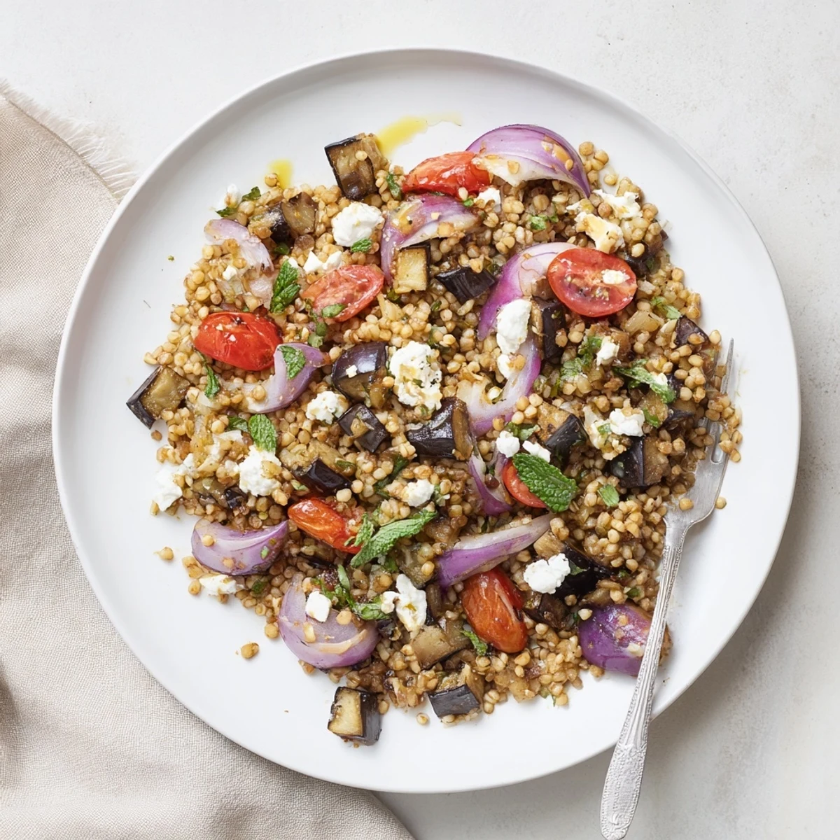 Golden brown roasted eggplant tossed with fluffy warm millet salad and fresh herbs in a white bowl