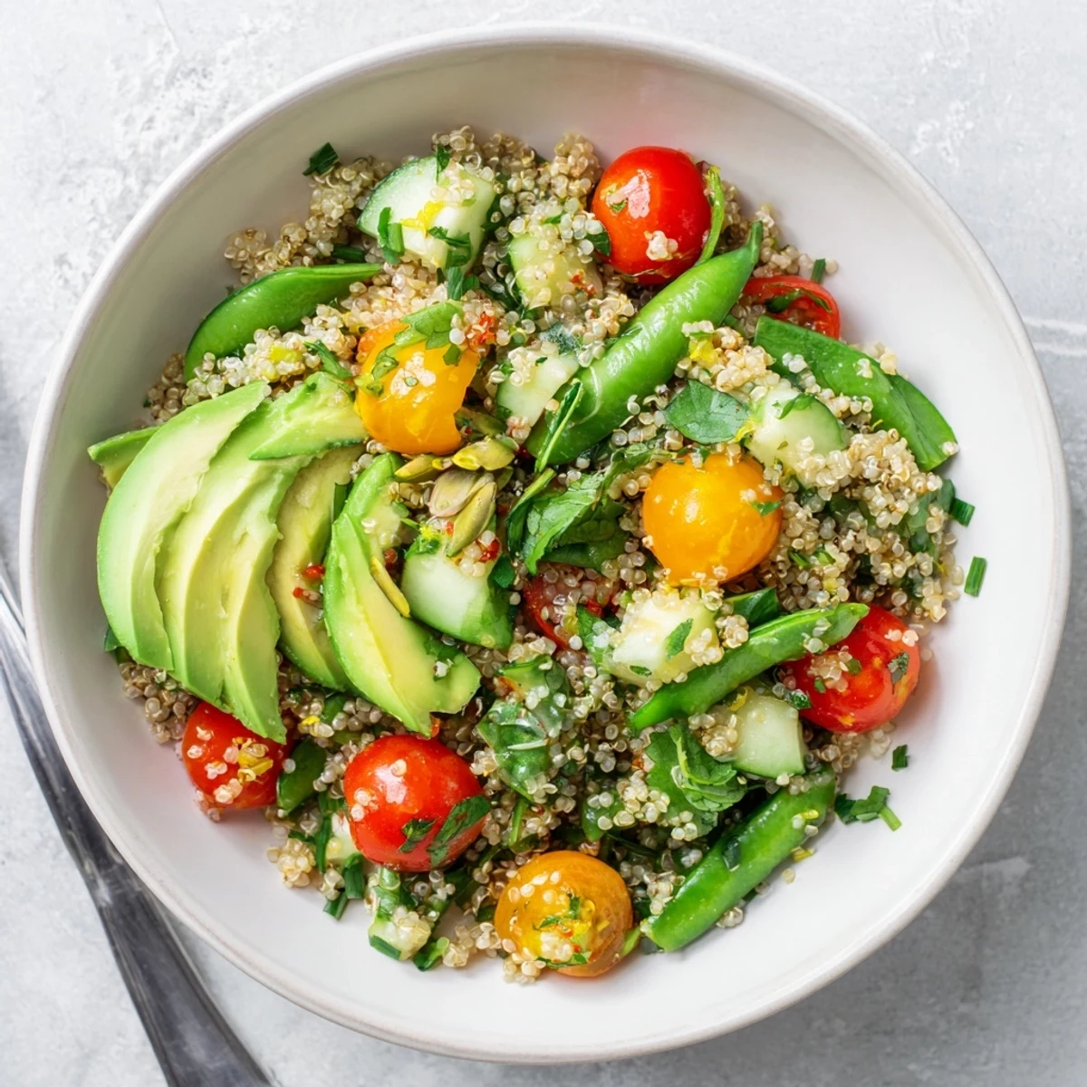 Citrus herb quinoa bowl featuring crisp snap peas, avocado slices, and vibrant vegetables drizzled with zesty vinaigrette