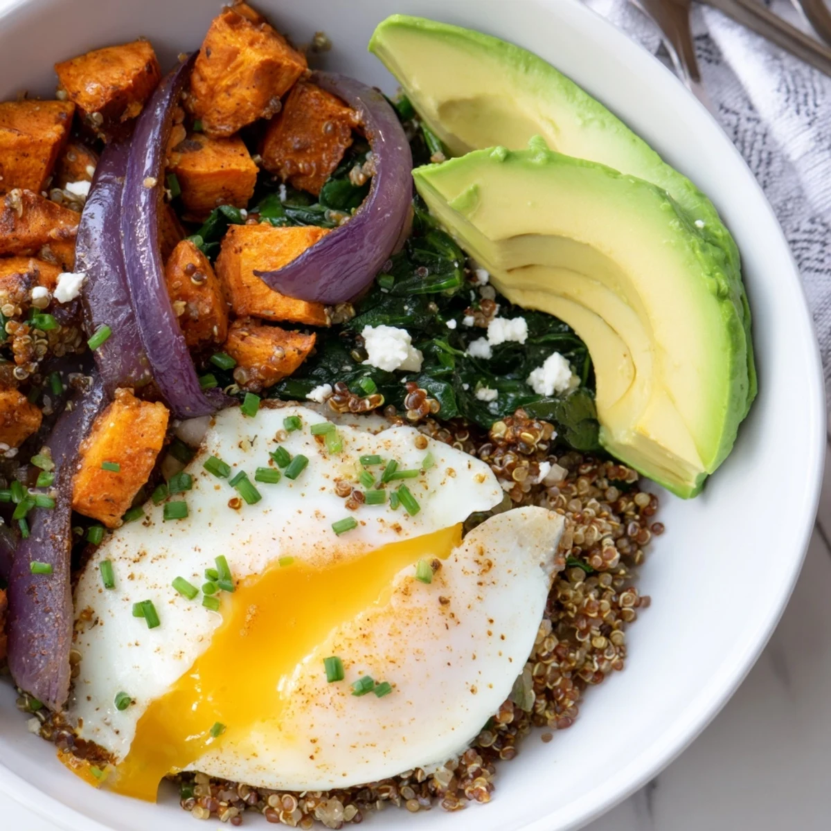 Golden quinoa breakfast bowl topped with roasted sweet potato cubes, wilted spinach, and a perfectly fried egg