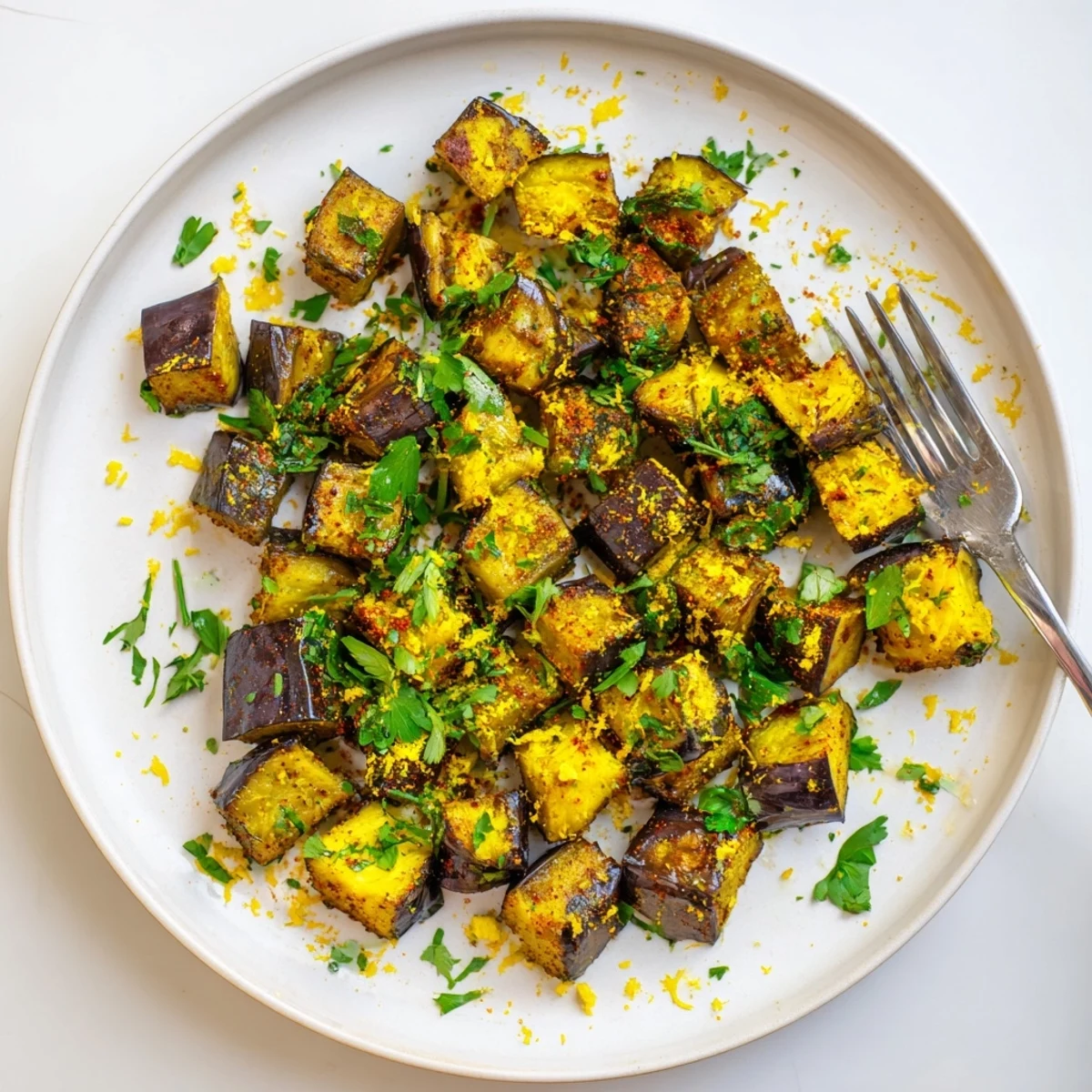 Golden brown smoky roasted eggplant cubes arranged on a white serving platter with fresh parsley garnish