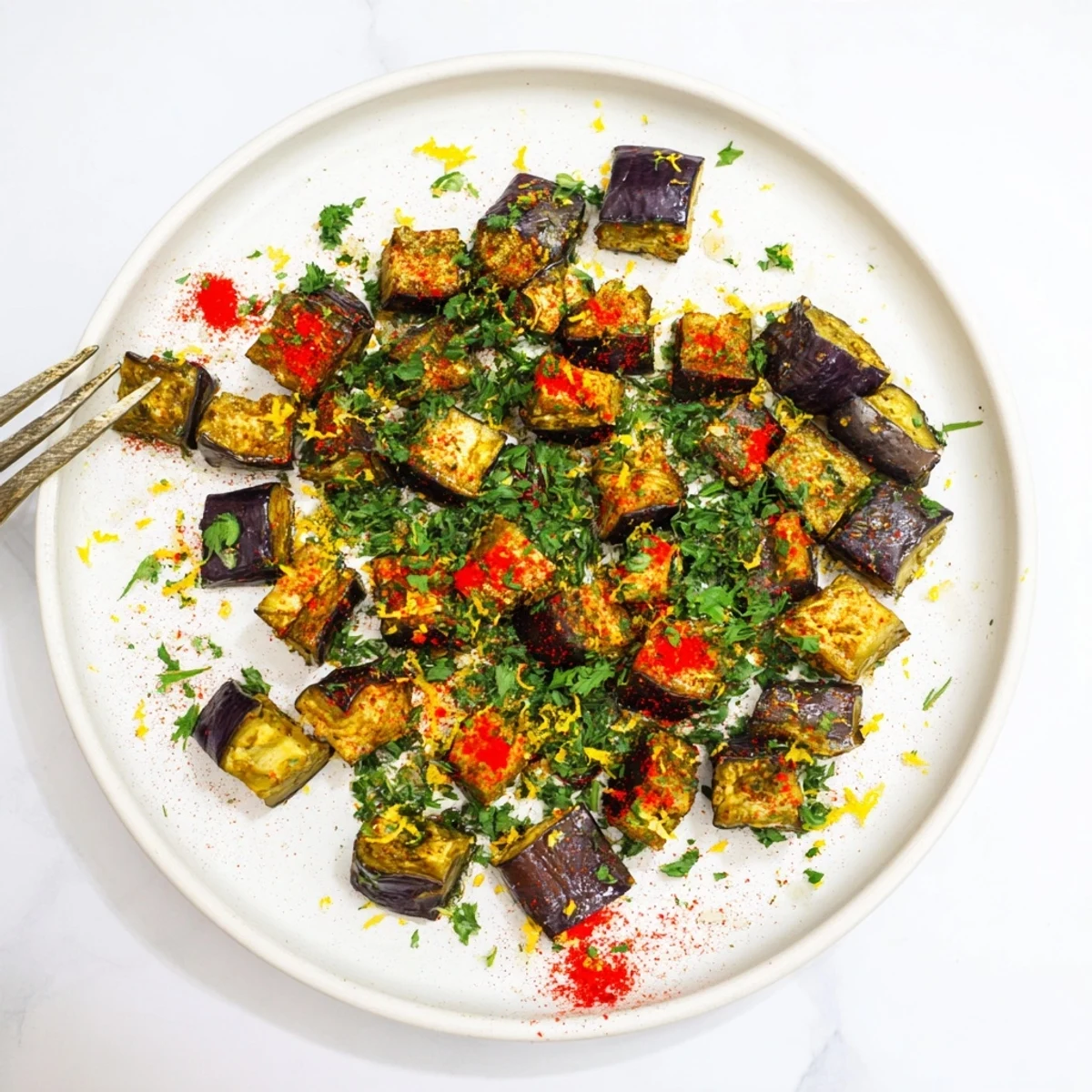 Close up of crispy edged roasted eggplant cubes topped with lemon zest on a rustic wooden board