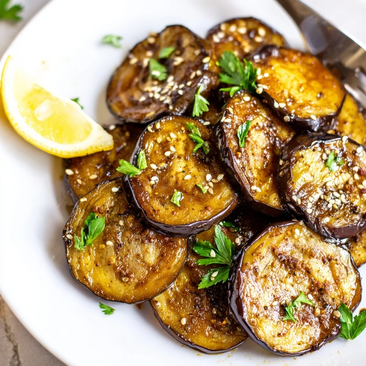 Warm Smoky Roasted Eggplant Coins topped with toasted sesame and lemon wedge.