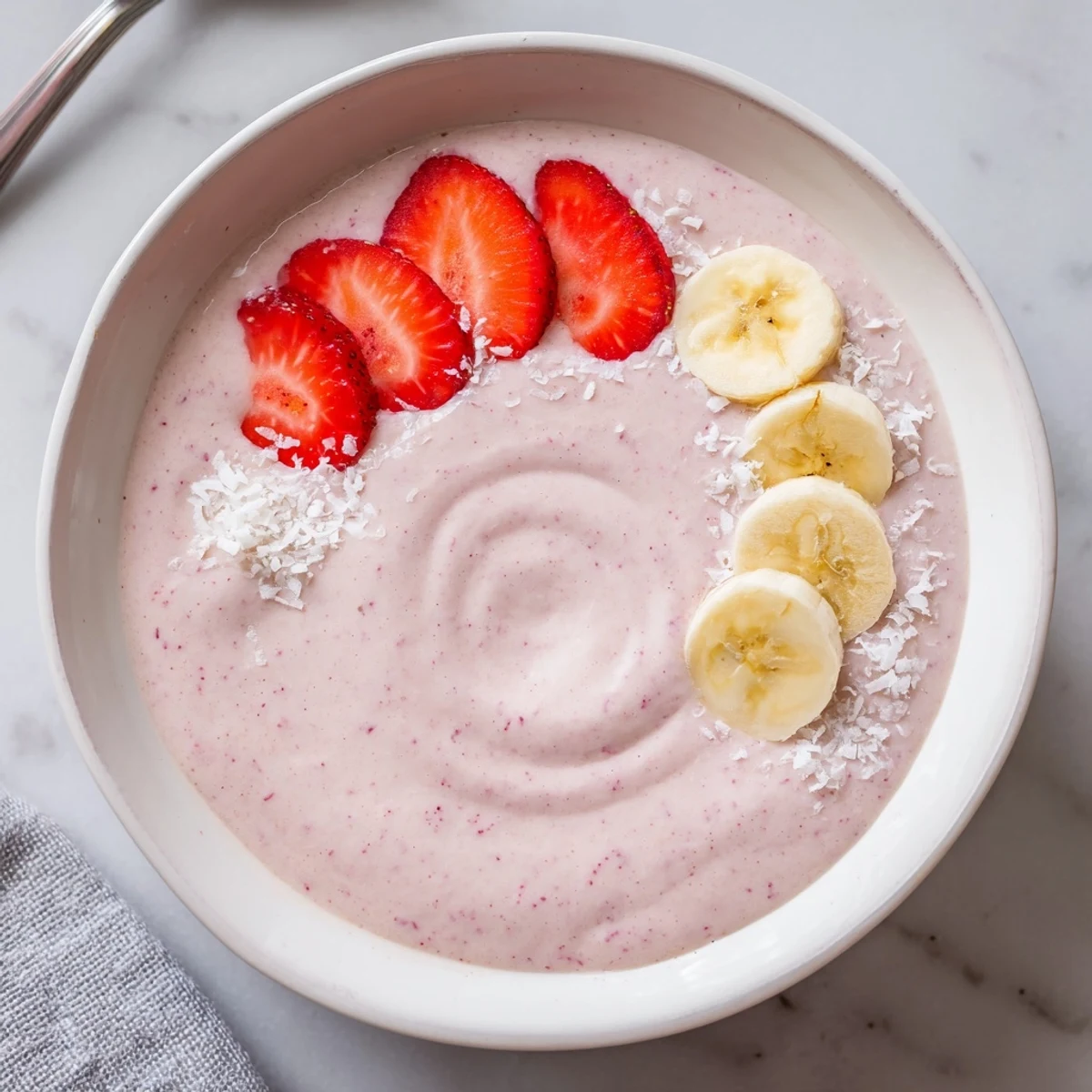 Thick Banana Strawberry Coconut Smoothie in bowl with sliced banana and strawberries.