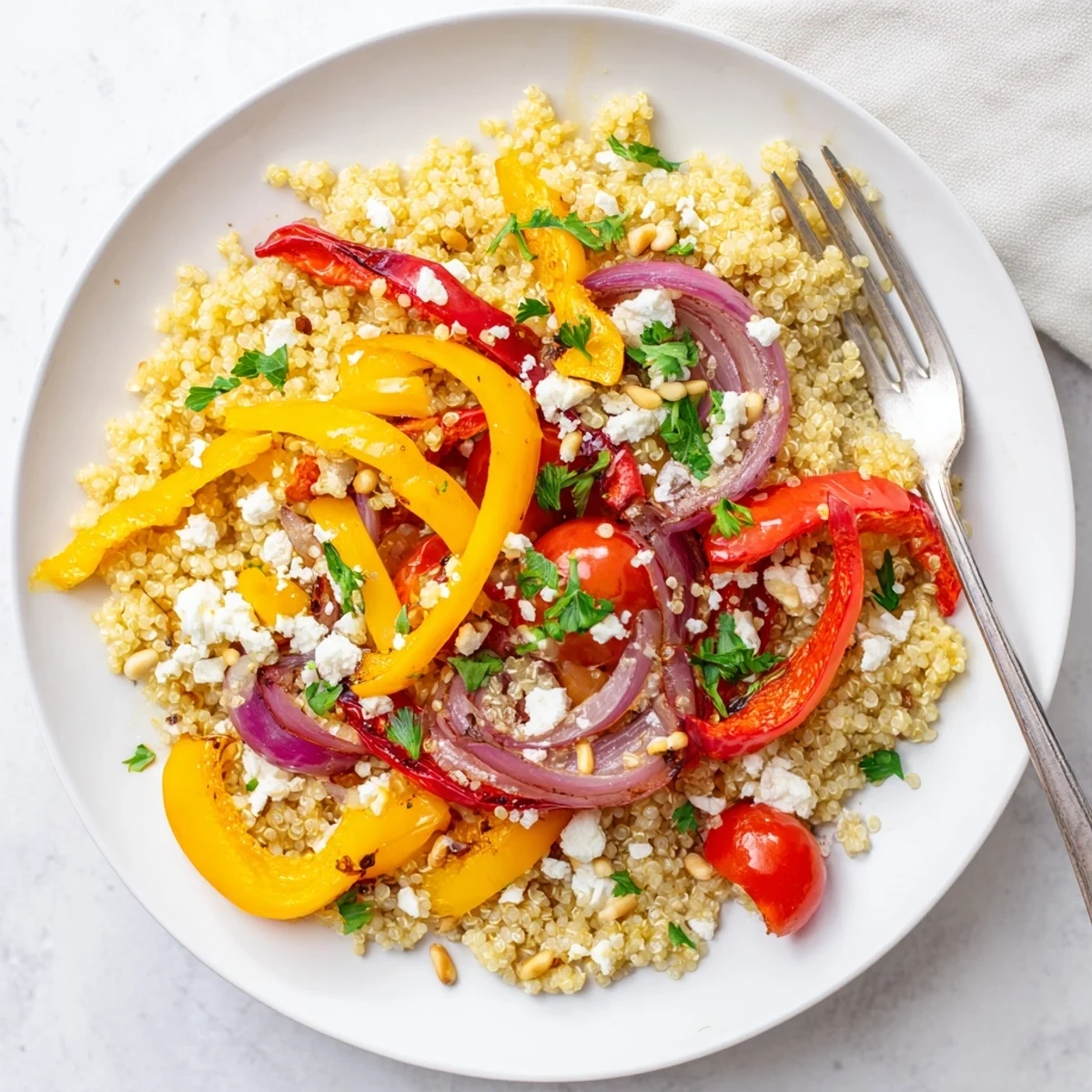 Fluffy quinoa mixed with sweet roasted peppers and zesty lemon dressing in white bowl
