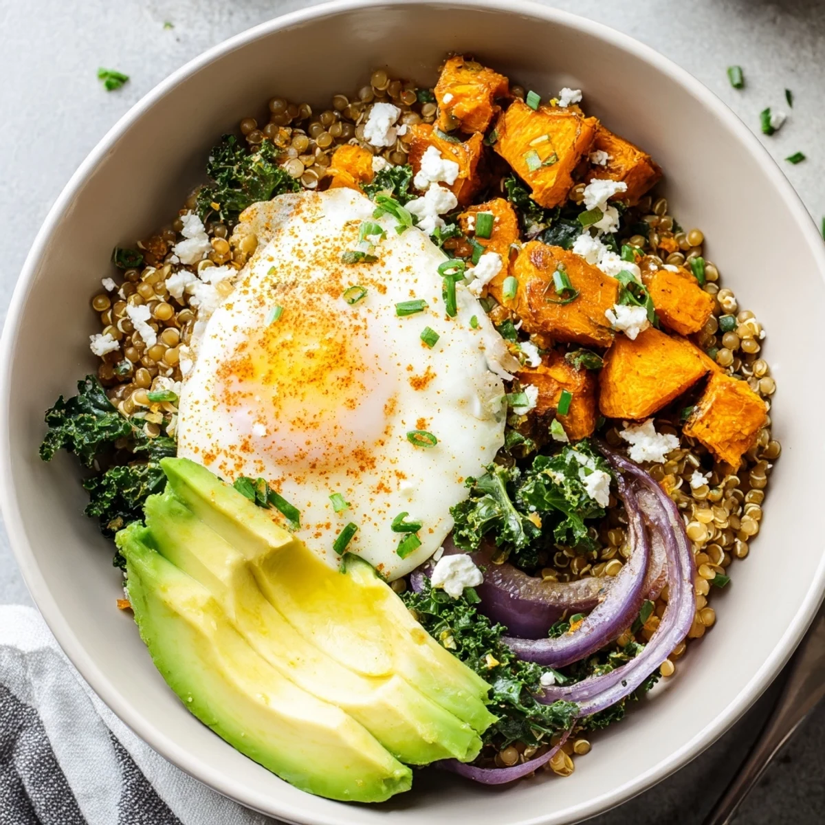 Warm sweet potato and kale sorghum breakfast bowl topped with a runny egg and crumbled feta cheese