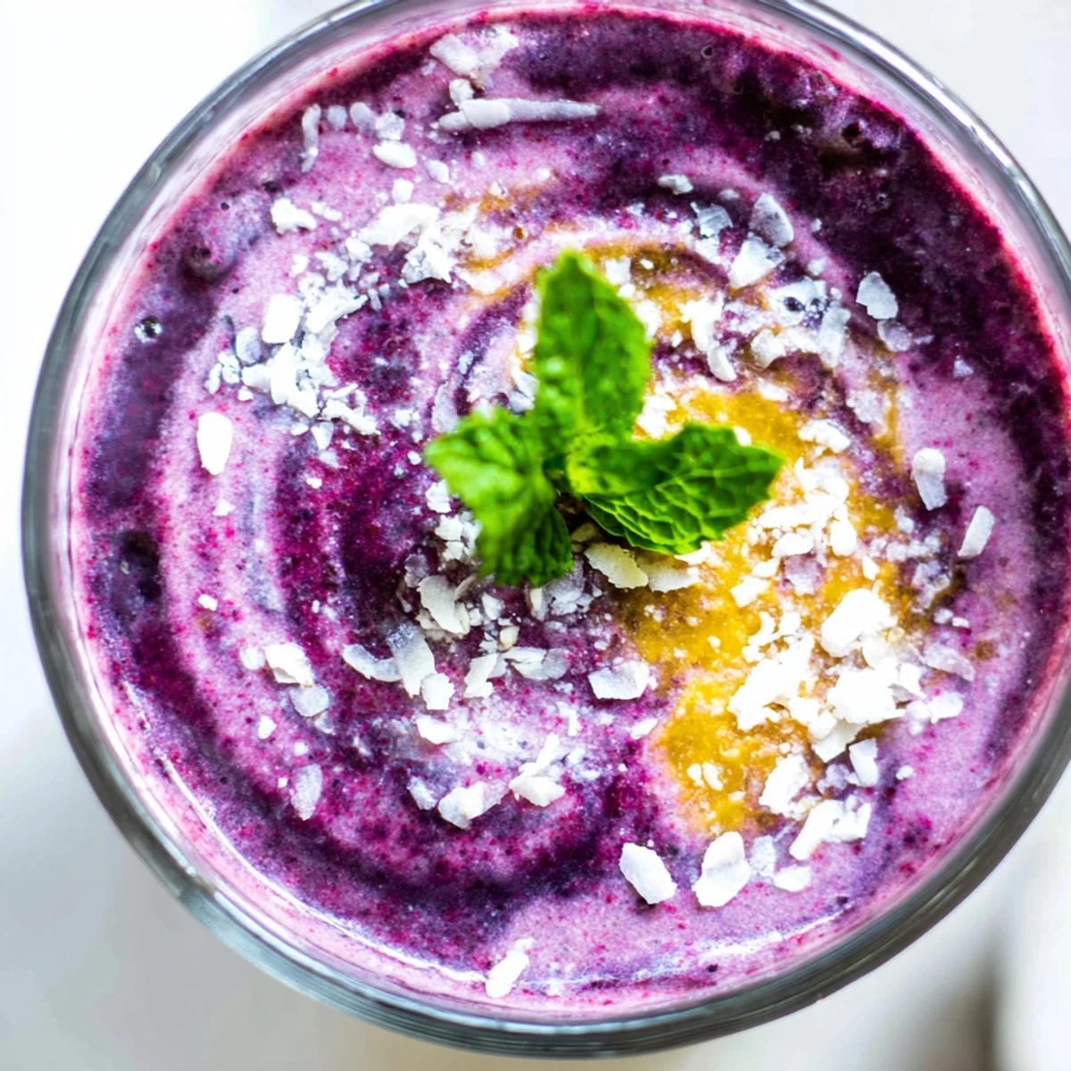 A vibrant blueberry peach coconut smoothie topped with shredded coconut and fresh mint in a clear glass.