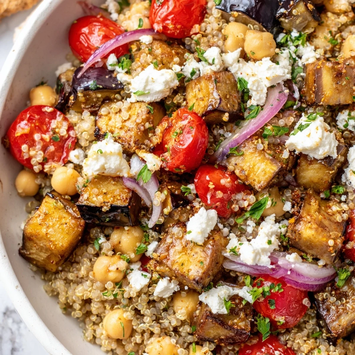 Mediterranean roasted eggplant quinoa grain bowl topped with crumbled feta and fresh herbs