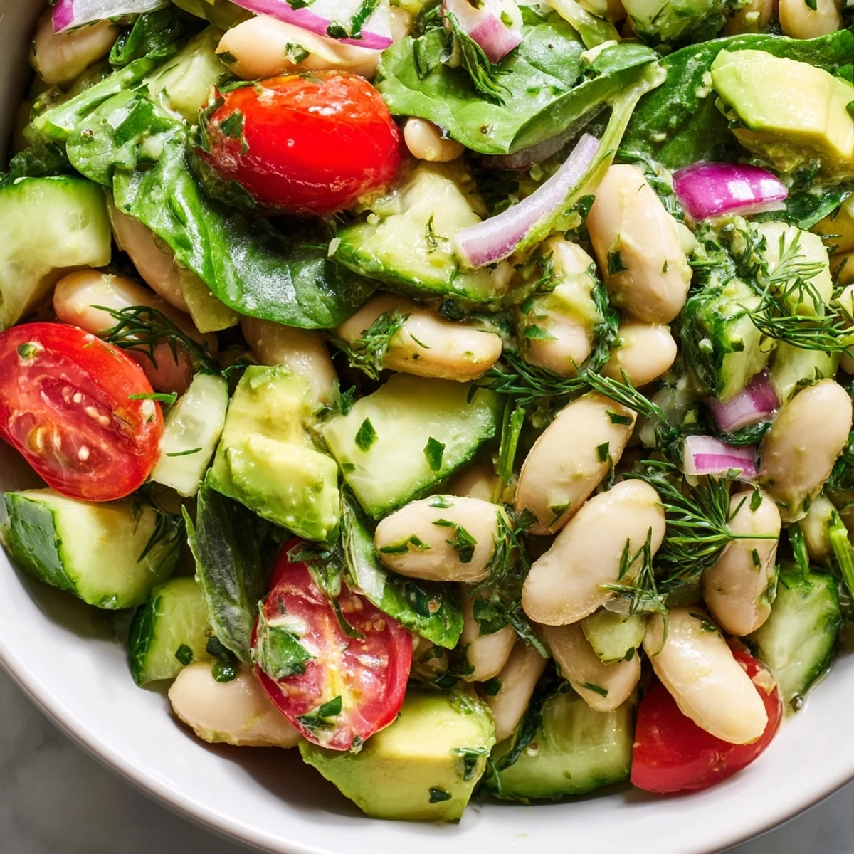 Creamy avocado dill white bean salad bowl topped with ripe tomatoes and fresh herbs