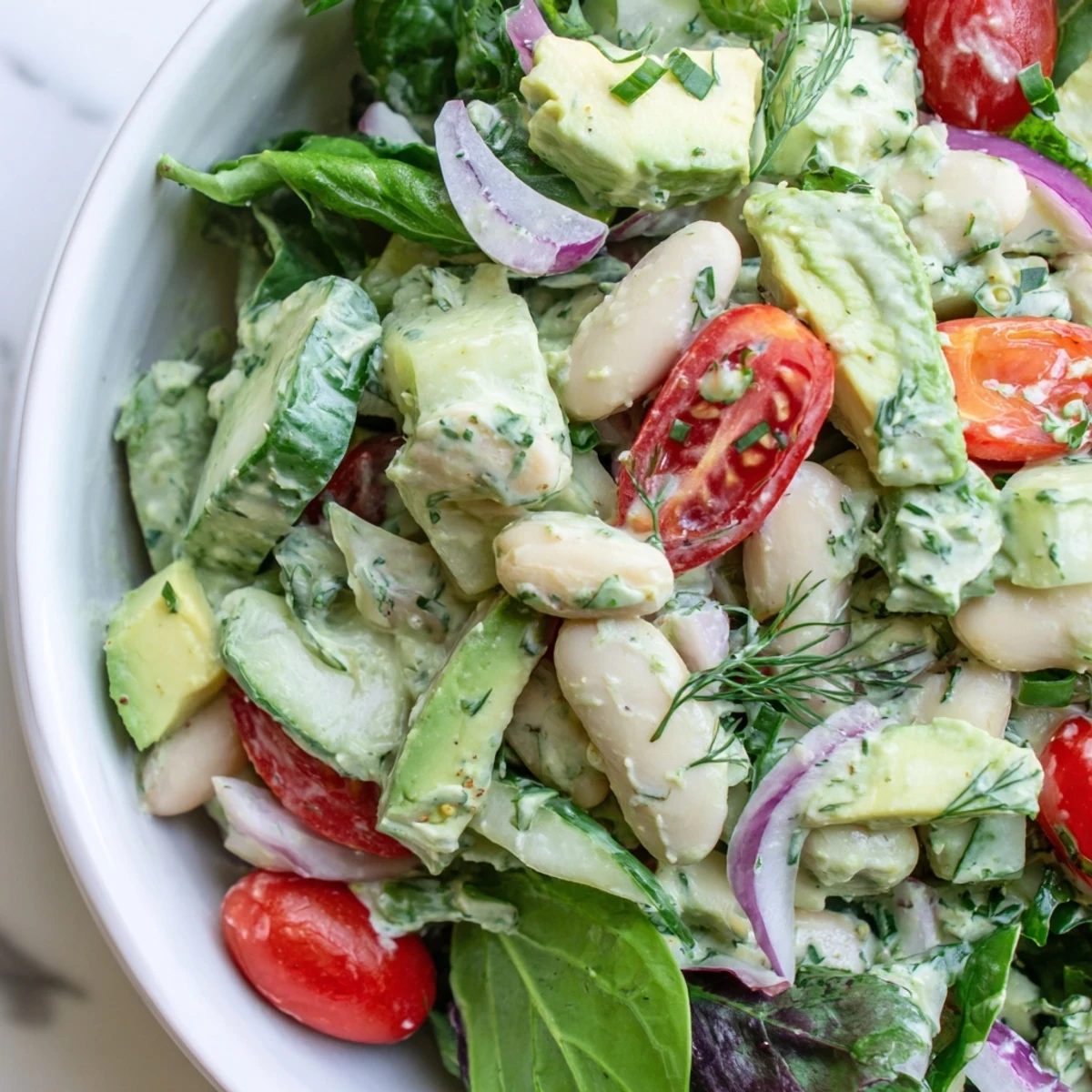 A vibrant white bean salad bowl layered with creamy avocado, dill dressing, and greens