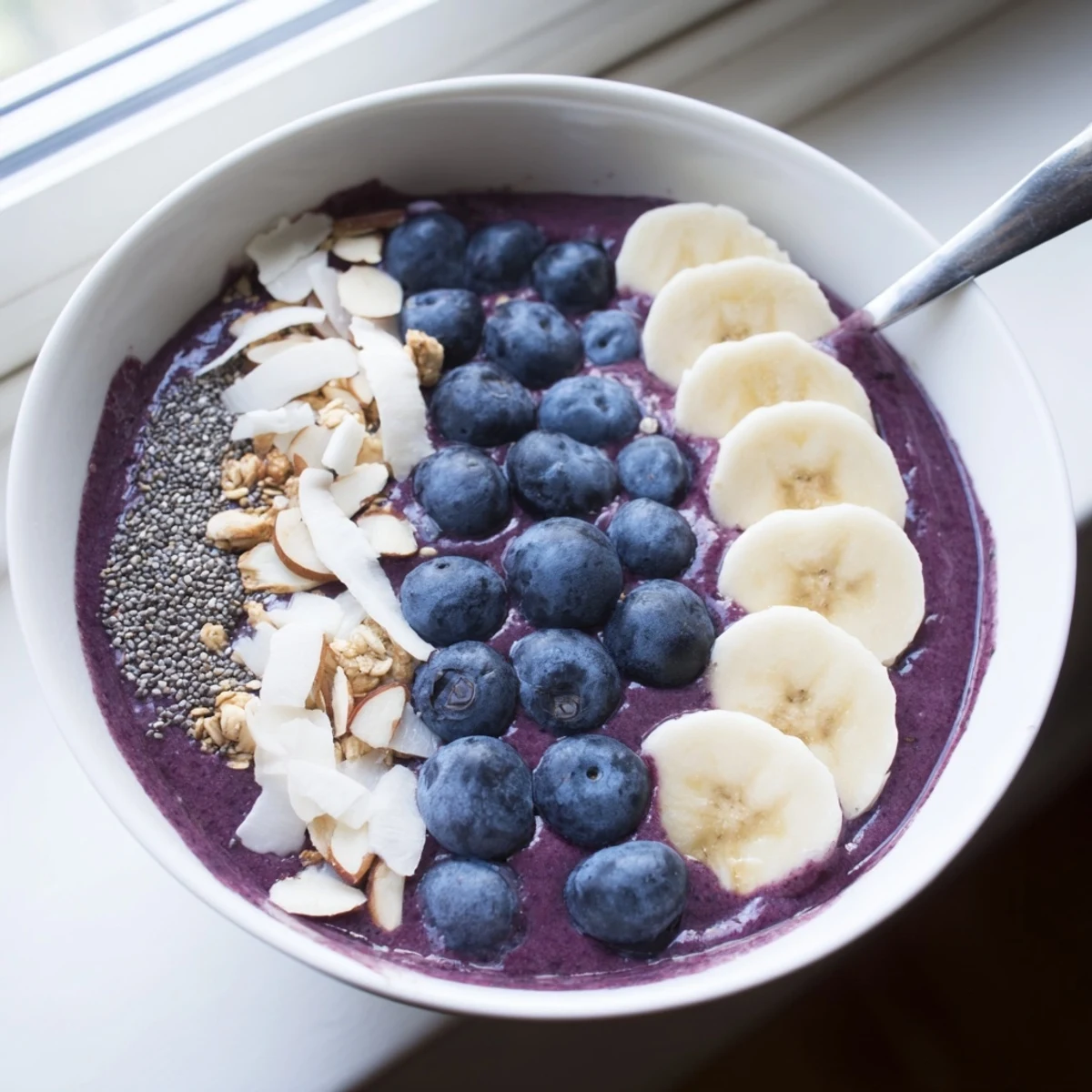 Thick Blueberry Banana Almond Smoothie Bowl crowned with sliced banana, almonds, and toasted coconut