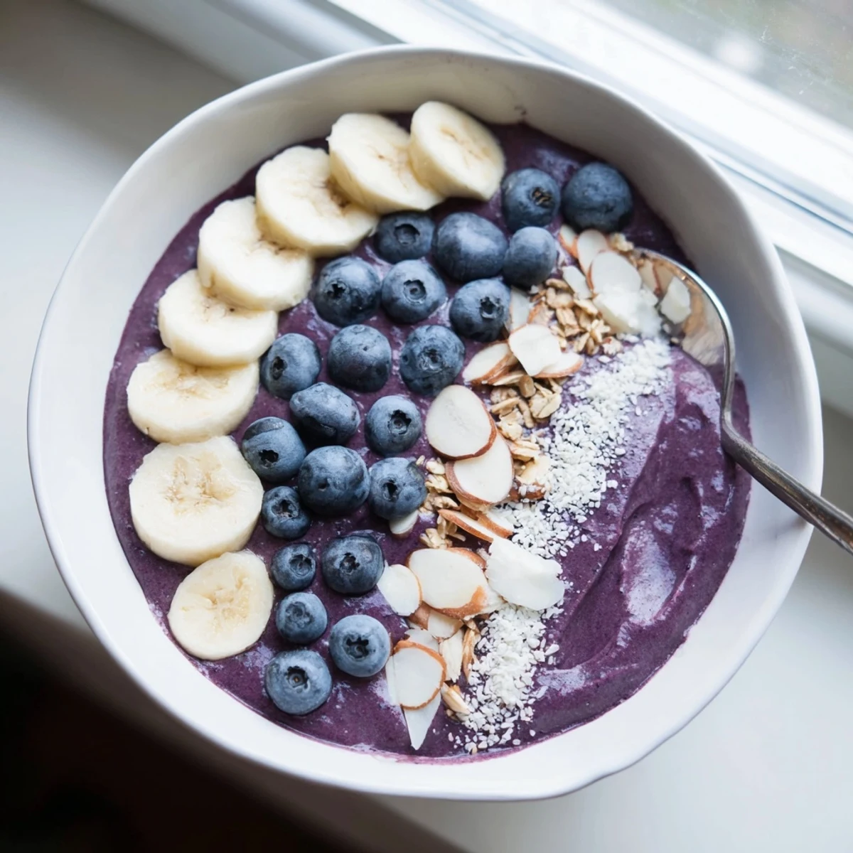 Creamy purple Blueberry Banana Almond Smoothie Bowl topped with coconut flakes and fresh fruit