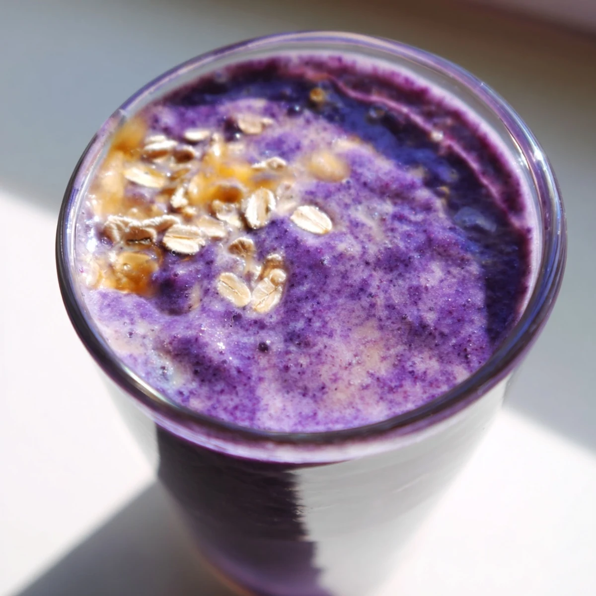 Purple blueberry mango oat smoothie poured into a glass with fresh berries on top