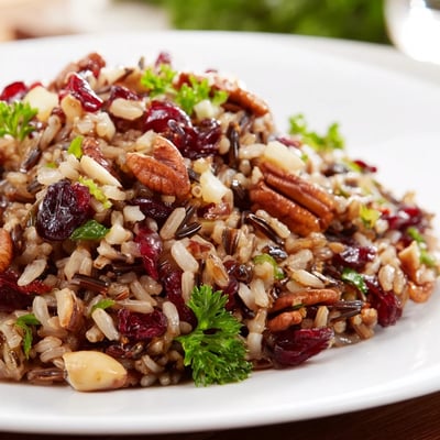 Spoon serving of warm Hearth Baked Nutty Wild Rice and Cranberry Medley next to roasted chicken on a rustic table.